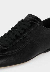 Μαύρο δερμάτινο παπούτσι με κορδόνια, υφή, στρογγυλεμένη μύτη και διακριτικές ραφές στο πλάι και στη γλώσσα.