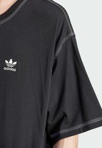 Črna kratkosleeva majica iz bombažnega blaga z belim kontrastnim šivom in izvezenim Adidasovim logotipom na levem prsnem delu.