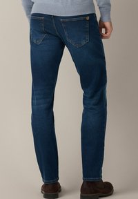 Ciemnoniebieskie dżinsy o slim fit z klasycznym pięciopocketowym fasonem i brązowym przeszyciem, noszone z jasnoszarym swetrem.