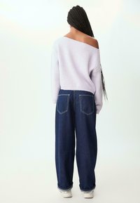 Ljuslila ribbstickad off-the-shoulder-tröja i kombination med löst sittande mörkblå denimjeans med två bakfickor och uppvikta ärmar.