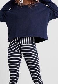Sudadera corta de color navy con mangas largas, combinada con leggings a rayas en navy y blanco que cuentan con una cinturilla alta y un diseño ajustado.