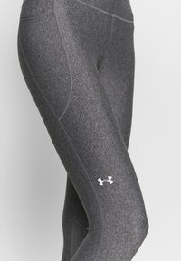 Grå sportleggings har en texturerad tyg, släta sömmar och en vit Under Armour-logga på underbenet.