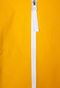 Żółty strój na zamek błyskawiczny o gładkiej fakturze, wyposażony w biały zamek i uchwyt. Projekt zawiera detale szwów na przodzie.