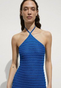 Blue halter dress made of textured fabric with horizontal pleats. Features thin straps and a fitted silhouette.