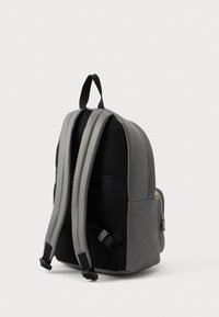 Grå rygsæk lavet af tekstureret stof med polstrede skulderstropper og et geometrisk mønster på siden. Lynlåslomme synlig.