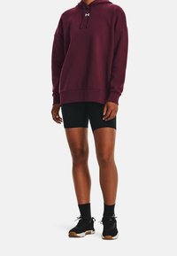 Haut à capuche bordeaux avec poche devant, short de cyclisme noir et baskets noires avec semelles blanches et accents marron. Matériau doux, coupe décontractée.