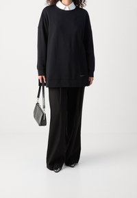 Czarny sweter z okrągłym dekoltem i opadłymi ramionami, w połączeniu z szerokimi czarnymi spodniami. Zawiera mały detal logo i teksturowaną torebkę.