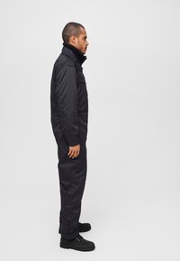 Black one-piece jumpsuit with a high collar, long sleeves, and zippered pockets; made from a durable fabric with a smooth texture.