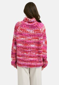Übergroßer Pullover mit einem Schalkragen und einem mehrfarbigen Strickmuster in den Farbtönen Rosa, Rot und Weiß mit einer strukturierten Oberfläche.