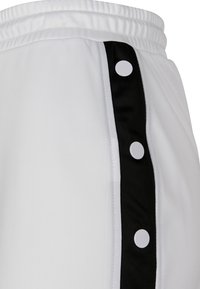 Pantalones cortos deportivos blancos con un panel lateral negro y botones a presión. Textura de tela suave con cintura elástica.