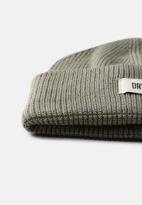 Olive green knit beanie with a ribbed texture and a folded cuff. Features a white label with black text on the side.