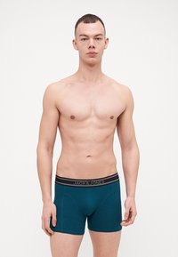 Türkise Boxershort mit schwarzem Bund, auf dem "JACK & JONES" steht. Sie zeigen ein figurbetontes Design und eine glatte Textur.