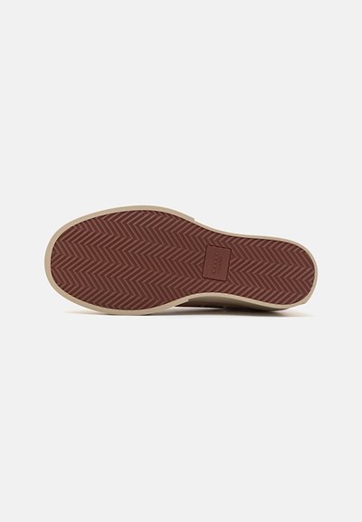 Brun gummisula med ett strukturerat fiskbensmönster, med en beige kant och en rektangulär logotyp i mitten.