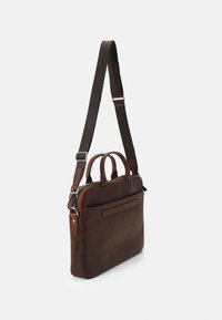 Bandolera de cuero marrón con dos asas y una correa larga ajustable. Cuenta con un bolsillo delantero y un diseño elegante y minimalista.