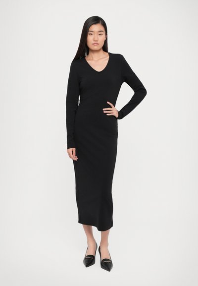 Long black dress made of stretchy fabric, featuring a V-neckline and long sleeves, with a slim-fit silhouette and side slits for ease of movement.