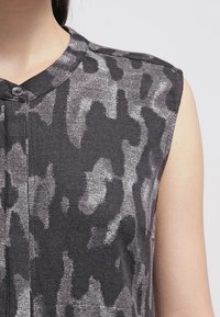 Sleeveless top with a high neckline, featuring a dark gray and silver camouflage pattern. Made of a soft, textured fabric with front buttons.