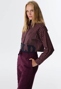 Korte geruite blouse in rood en marineblauw met een knoopsluiting, gecombineerd met donkerpaarse joggingbroek met geborduurde details en een trekkoord.