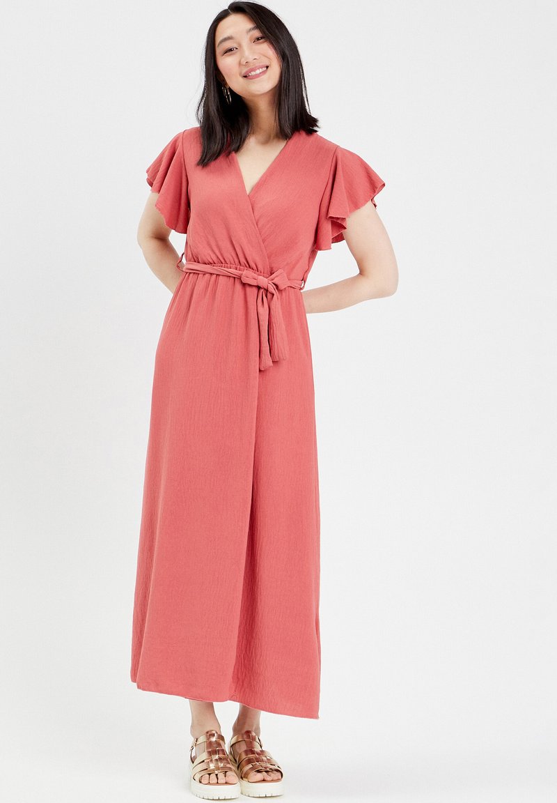 Robe portefeuille en corail avec des manches flottantes, taille ceinturée et longueur cheville. Fabriquée en tissu froissé avec une finition texturée.