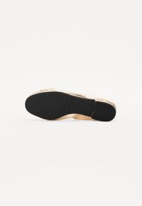 Chaussure plate dorée avec une texture lisse, dotée d'une semelle en caoutchouc noir avec des rainures horizontales. Le talon est minimal, offrant un design élégant.