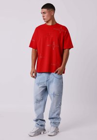 Rode, oversized t-shirt met sterrenpatronen en geborduurde details; gecombineerd met lichtblauwe denim broek met stervormige patches en een relaxte pasvorm.