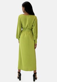 Robe mi-longue à manches longues de couleur vert vif, confectionnée dans un tissu lisse. Dispose d'une taille cintrée avec ceinture, d'une silhouette fluide et d'une coupe décontractée.
