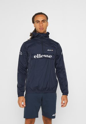 Navy windbreaker jacket with elastic cuffs, front logo print, and hood. Paired with dark shorts, showcasing a sporty, casual design.