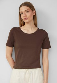 T-shirt marron à manches courtes avec un col rond, fabriqué en matériau doux, offrant un design ajusté. Texture lisse, style minimaliste.