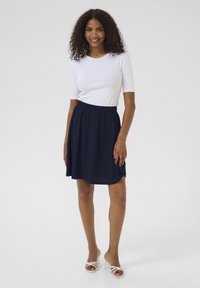 Jupe marine avec une taille élastique, longueur genou, en tissu léger. Associée à un haut blanc ajusté et des sandales à talons blocs blanches.