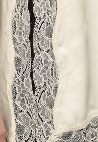 Gros plan d'un tissu en dentelle crème avec des motifs floraux sur fond noir et un textile en satin crème lisse.