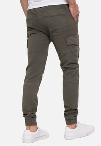 Cargo bukser i olivengrøn, lavet af bomuld, har flere lommer, ribbede manchetter og et tapered design. Sammen med hvide sneakers.