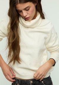 Cremfarbener Pullover mit Cowl-Neck und gerippter Textur, in lässigem Schnitt mit langen Ärmeln und kontrastierenden schwarzen Akzenten an den Bündchen.