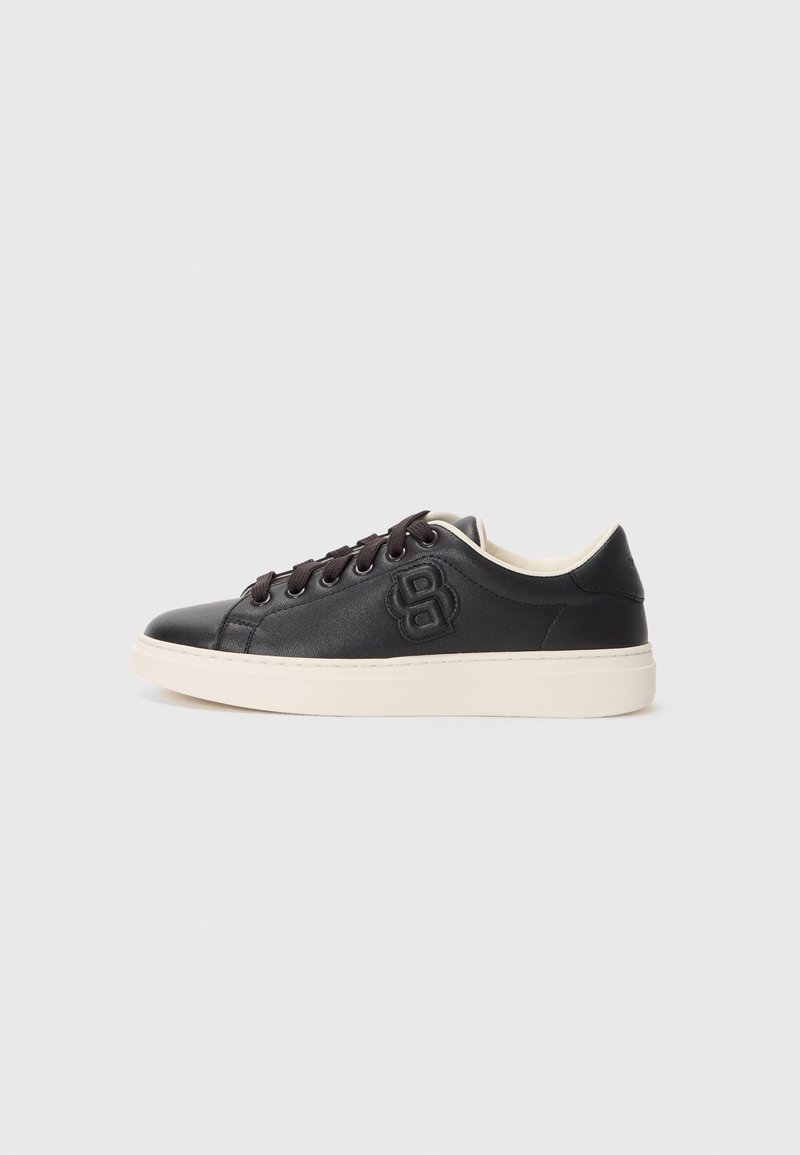 Sorte lær sneakers med rund tå, kontrasterende kremfarget såle, mørke snørebånd og preget logo detalj på siden. Jevn tekstur generelt.