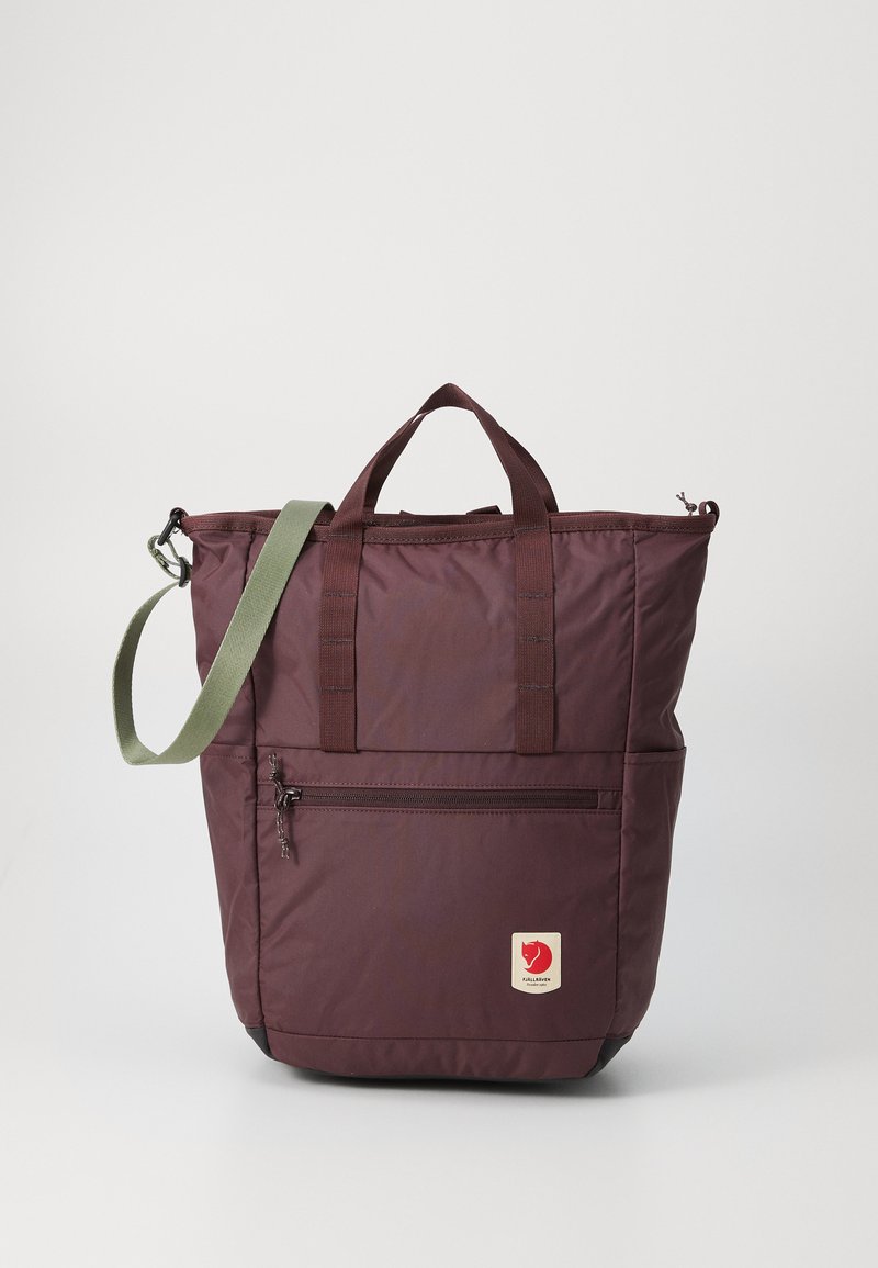 Bolso tote burdeos con cremallera en la parte superior, correa de hombro verde y bolsillo frontal. Presenta un parche con logo y material de nylon texturizado.