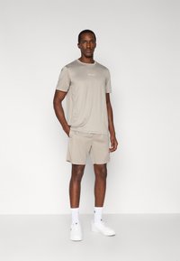 Μπεζ αθλητική εμφάνιση που αποτελείται από κοντομάνικη μπλούζα και σορτς, και τα δύο από λείο ύφασμα. Φοριέται με λευκά αθλητικά παπούτσια και κάλτσες.