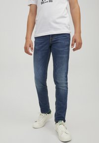 Kapeat siniset farkut, joissa on haalistuneita yksityiskohtia, yhdistetty valkoisiin lenkkareihin. Kangas on tekstuuri ja siinä on tyypillinen farkkukangasviimeistely.