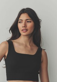 Black ribbed crop top with a square neckline and wide straps, featuring a textured fabric and a fitted, seamless design.