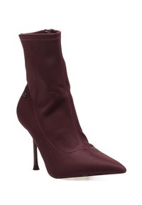 Botín de tobillo de tela elástica burdeos con puntera afilada, alto tacón de aguja y detalles de costura visibles. Cuenta con un cierre de cremallera lateral.