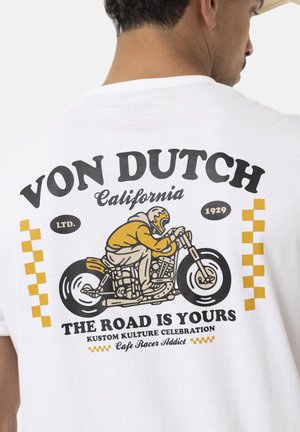 T-shirt blanc avec un graphique d'un motard en jaune et noir, orné de motifs à carreaux et du texte "LA ROUTE EST À VOUS."