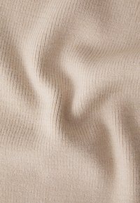 Beige ribstof die een zachte textuur toont met verticale lijnen, waardoor een zachte golfpatroon ontstaat. Het materiaal lijkt rekbaar en comfortabel.