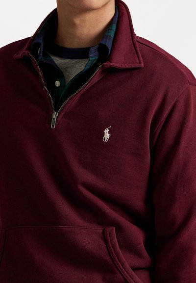 Bordeaux fleece pullover met een halve rits en gestikte vo pocket, met een wit geborduurd logo op de borst en een kraagontwerp.