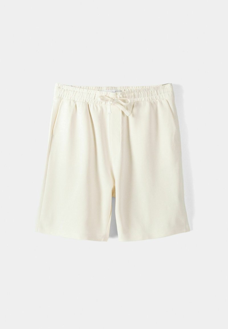 Shorts de sport de couleur crème, fabriqués dans un tissu lisse, avec une ceinture élastique munie d'un cordon de serrage réglable et des poches latérales.
