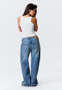 Falmede blå denim vide bukser med baglommer og en tan læderpatch; parret med en tætsiddende hvid tanktop.