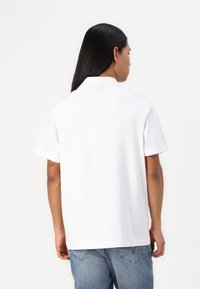 Balta īsām piedurknēm polo krekls ar klasisku apkakli, gluda tekstūra un brīva piegriezuma, apvienots ar gaiši ziliem džinsiem.