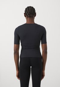 Sort, kortærmet, tætsiddende top med en glat tekstur. Har en rund halsudskæring og en cropped kant, parret med sorte leggings.