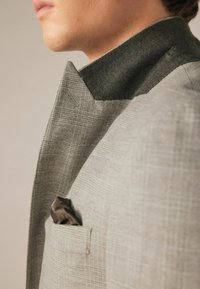 Grau karierter Blazer mit einem strukturierten dunklen Kragen und einem Einstecktuch. Verfügt über scharfe Revers und eine taillierte Passform, die modernes Design betont.