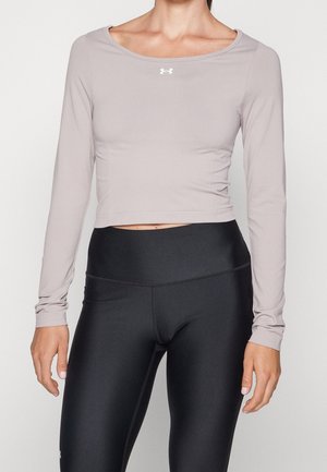 Femme portant un crop top à manches longues mauve clair et des leggings noirs taille haute, debout les bras détendus le long du corps.