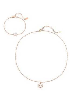 Delicate gold necklace and bracelet with fine chains, each featuring a round smiley face charm with a white background.