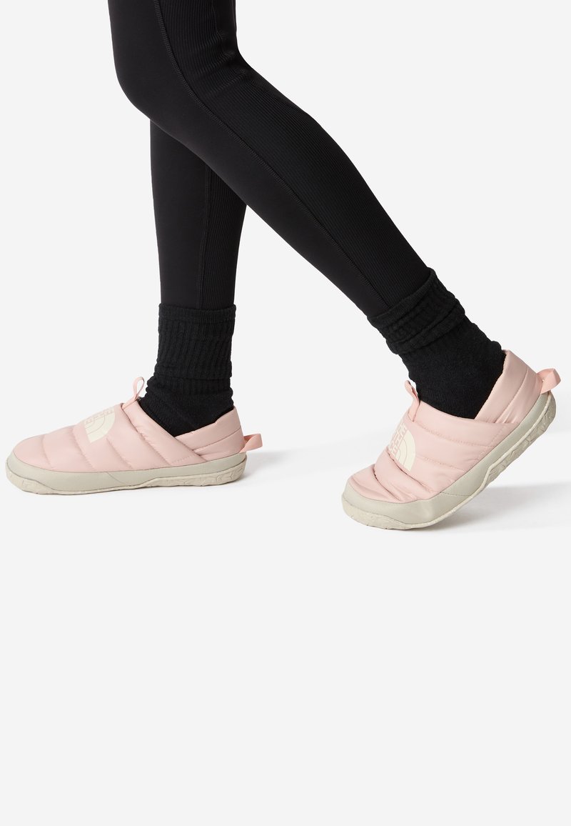Scarpe slip-on rosa imbottite con logo bianco, punta arrotondata e suola testurizzata, indossate con leggings neri e calze nere texturizzate.