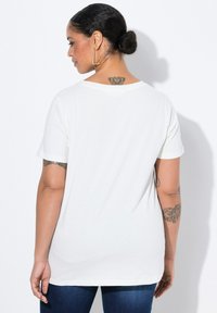 Camiseta blanca de manga corta con un ajuste relajado, cuello redondo y una textura suave. La vista trasera muestra un diseño sencillo y un acabado limpio.