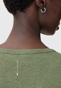 Olivengrøn t-shirt med en blød tekstur, der har et diskret logo-print på bagsiden nær halsudskæringen. Enkel, afslappet pasform.